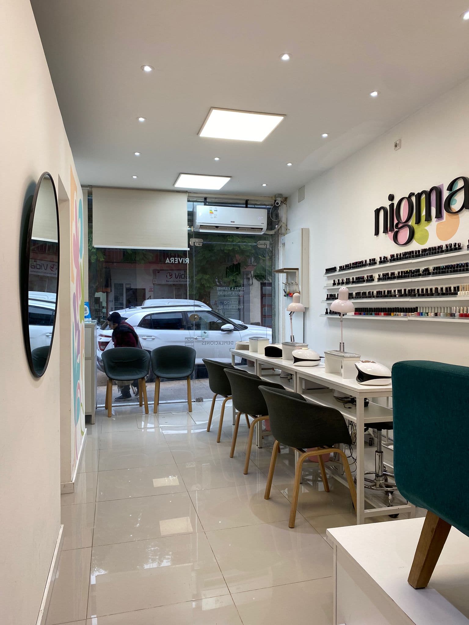 Interior del salón NIGMA: cabinas de manicuría con esmaltes y espejo redondo