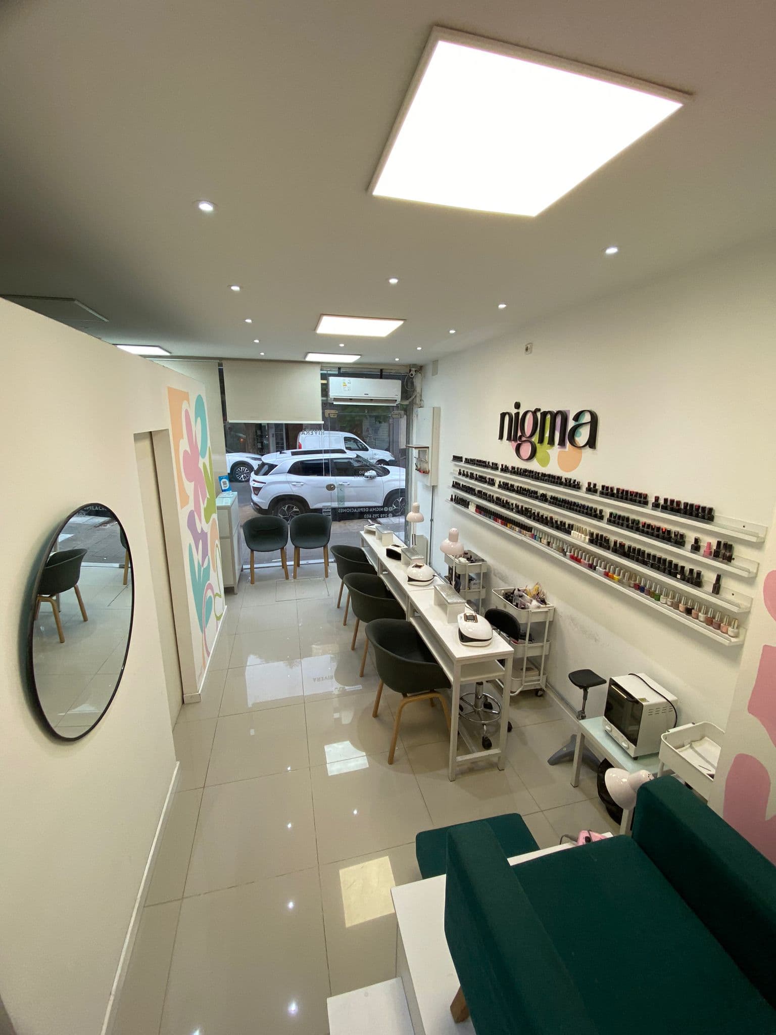 Interior del salón NIGMA: cabinas de manicuría con muro de esmaltes y panel LED en el techo